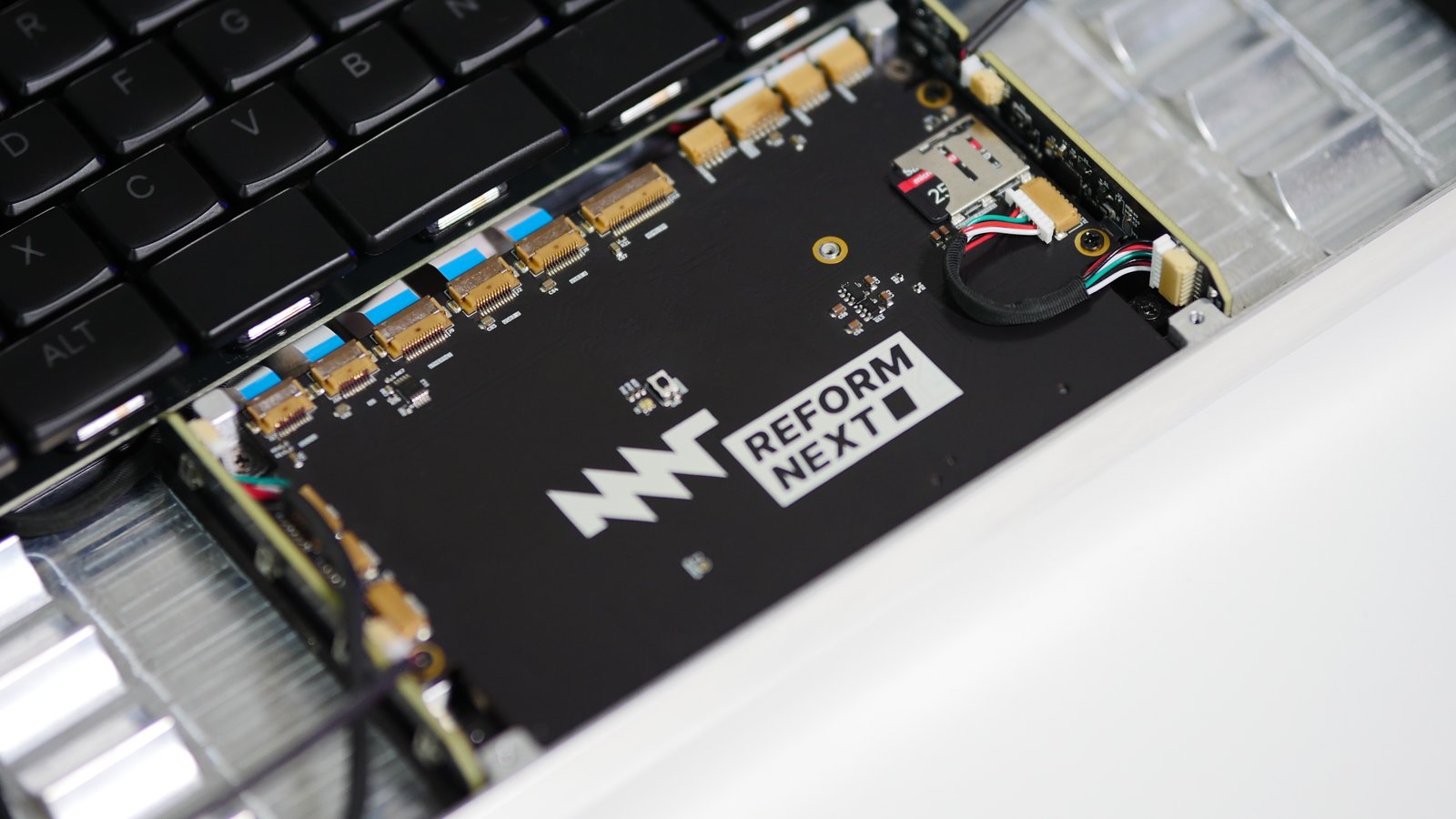 The motherboard installed inside an MNT Reform Next. It has a row of ribbon cable connectors at the top, and a small microSD card carrier visible to the left of an MNT Reform Next logo.